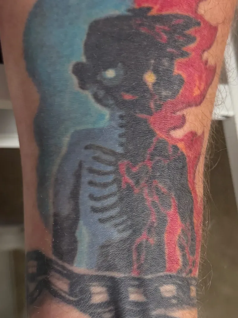 Andrew's left-forearm tattoo — a figure split between blue/ice and red/fire, wrapped by a film-strip band at the wrist